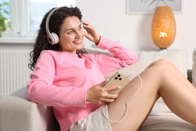 Photo of Young woman with headphones and smartphone listening to music at home