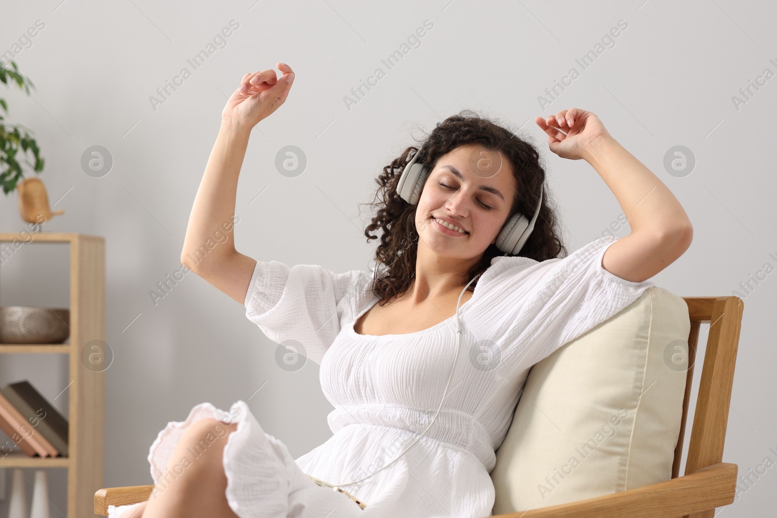 Photo of Young woman with headphones listening to music on armchair at home
