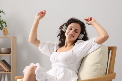Photo of Young woman with headphones listening to music on armchair at home