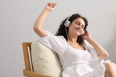 Photo of Young woman with headphones listening to music on armchair at home