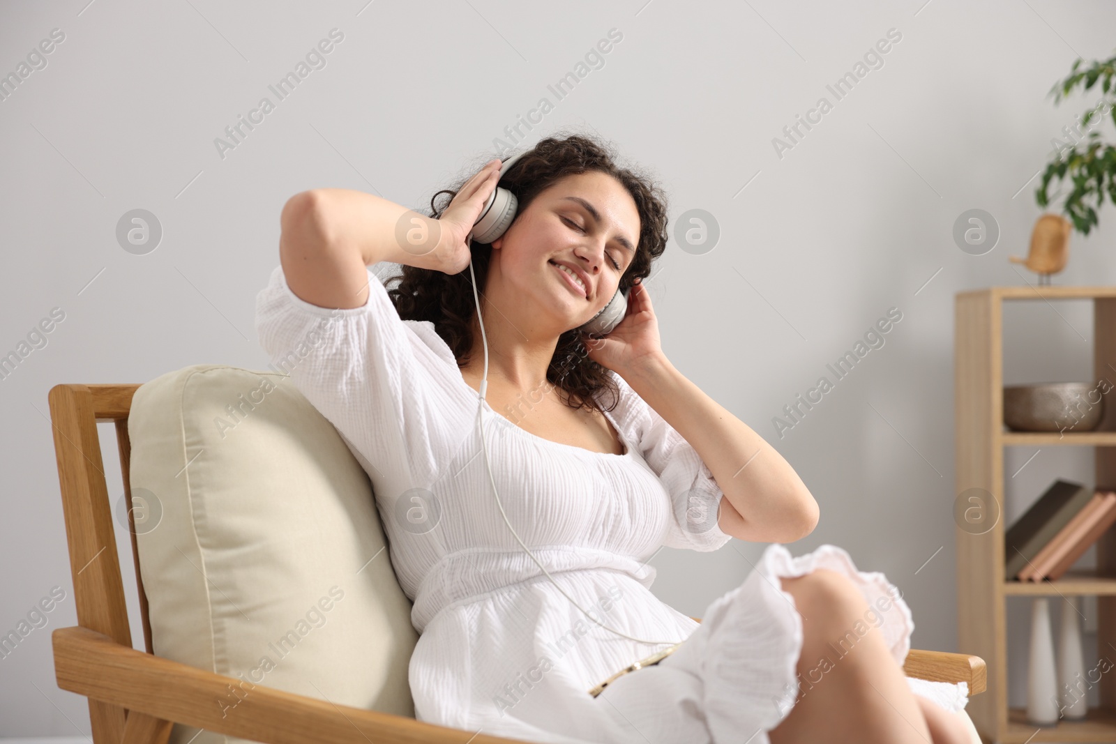 Photo of Young woman with headphones listening to music on armchair at home