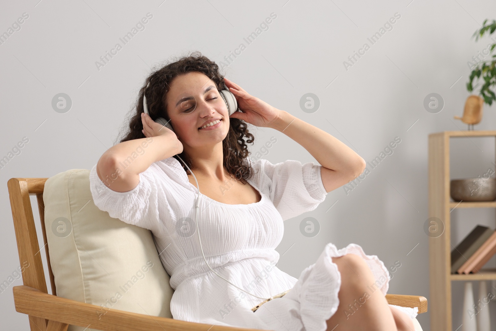 Photo of Young woman with headphones listening to music on armchair at home