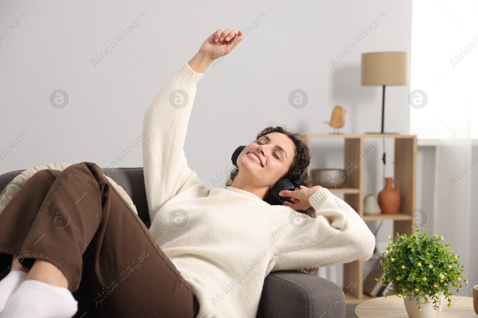 Photo of Young woman with headphones listening to music on armchair at home