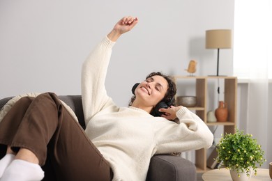 Photo of Young woman with headphones listening to music on armchair at home