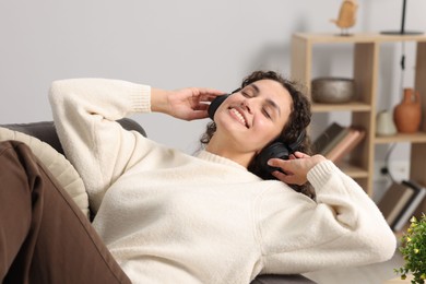 Photo of Young woman with headphones listening to music on armchair at home