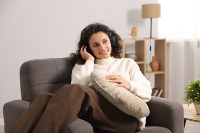 Photo of Young woman with headphones listening to music on armchair at home