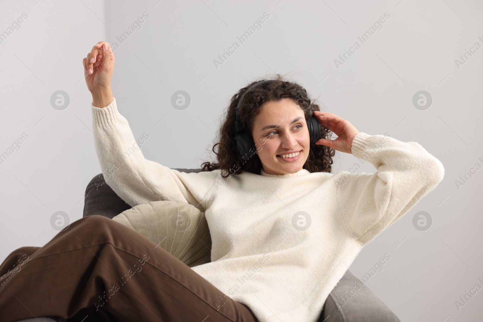 Photo of Young woman with headphones listening to music on armchair at home
