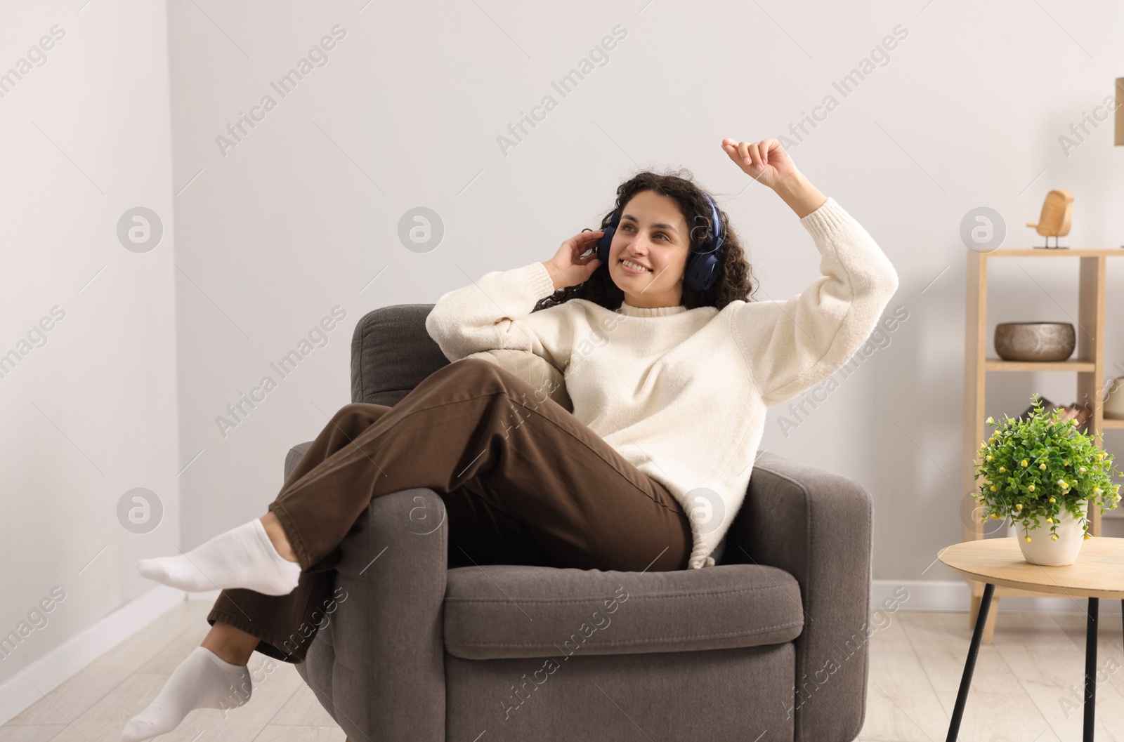 Photo of Young woman with headphones listening to music on armchair at home