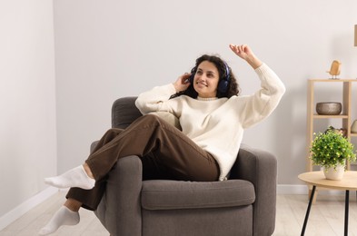Photo of Young woman with headphones listening to music on armchair at home