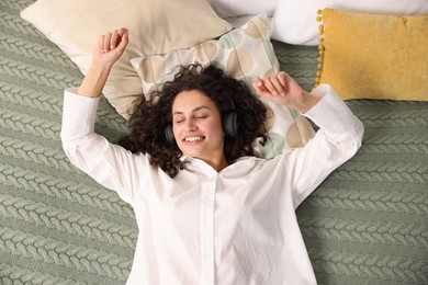 Photo of Young woman with headphones listening to music on bed at home, above view