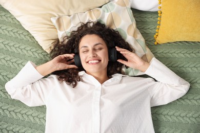 Photo of Young woman with headphones listening to music on bed at home, above view