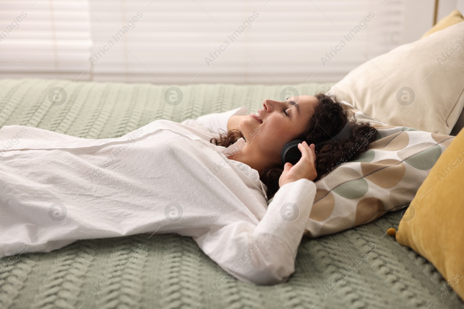Photo of Young woman with headphones listening to music on bed at home