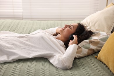 Photo of Young woman with headphones listening to music on bed at home