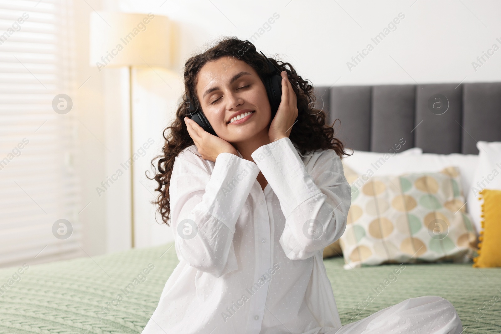 Photo of Young woman with headphones listening to music on bed at home