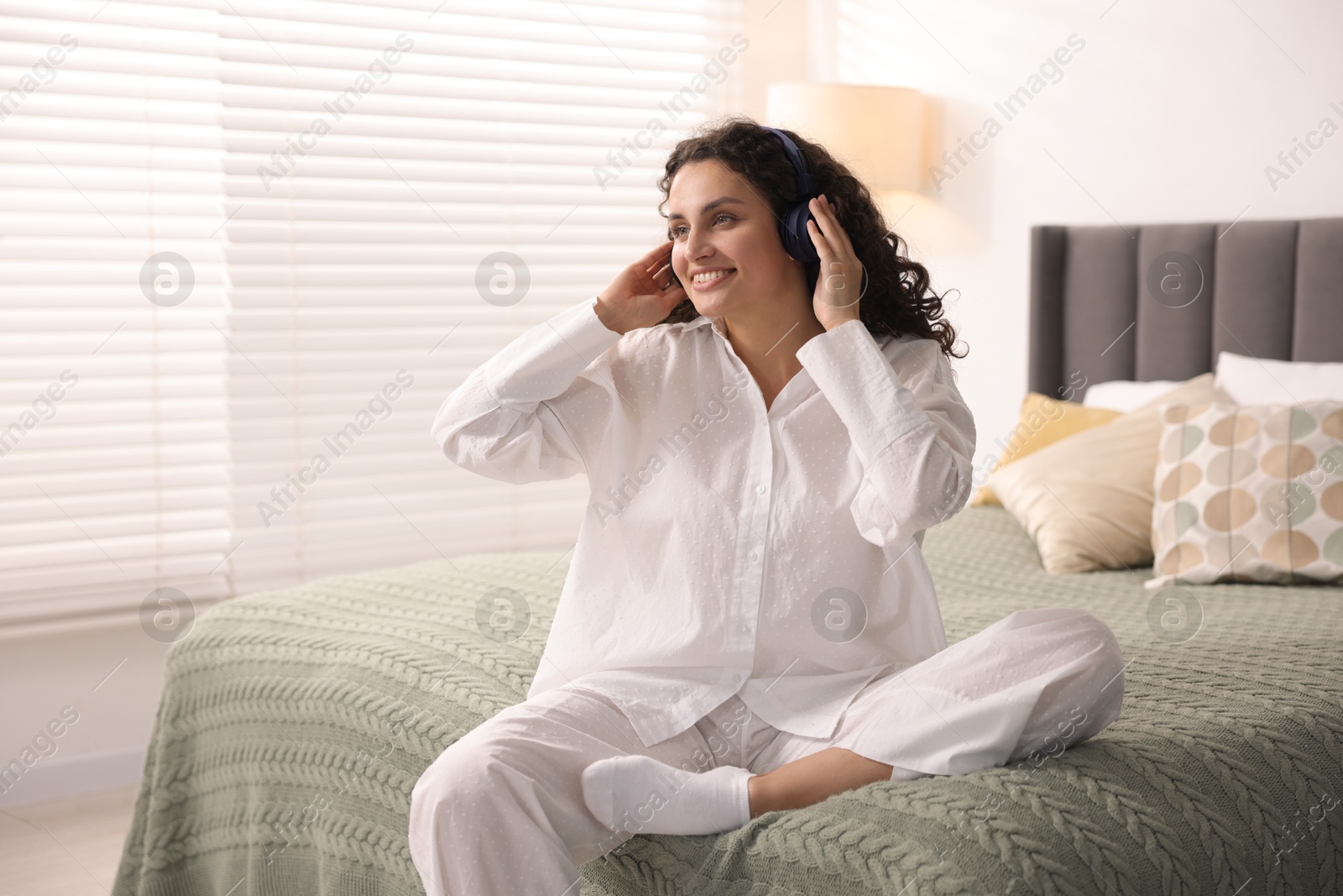 Photo of Young woman with headphones listening to music on bed at home