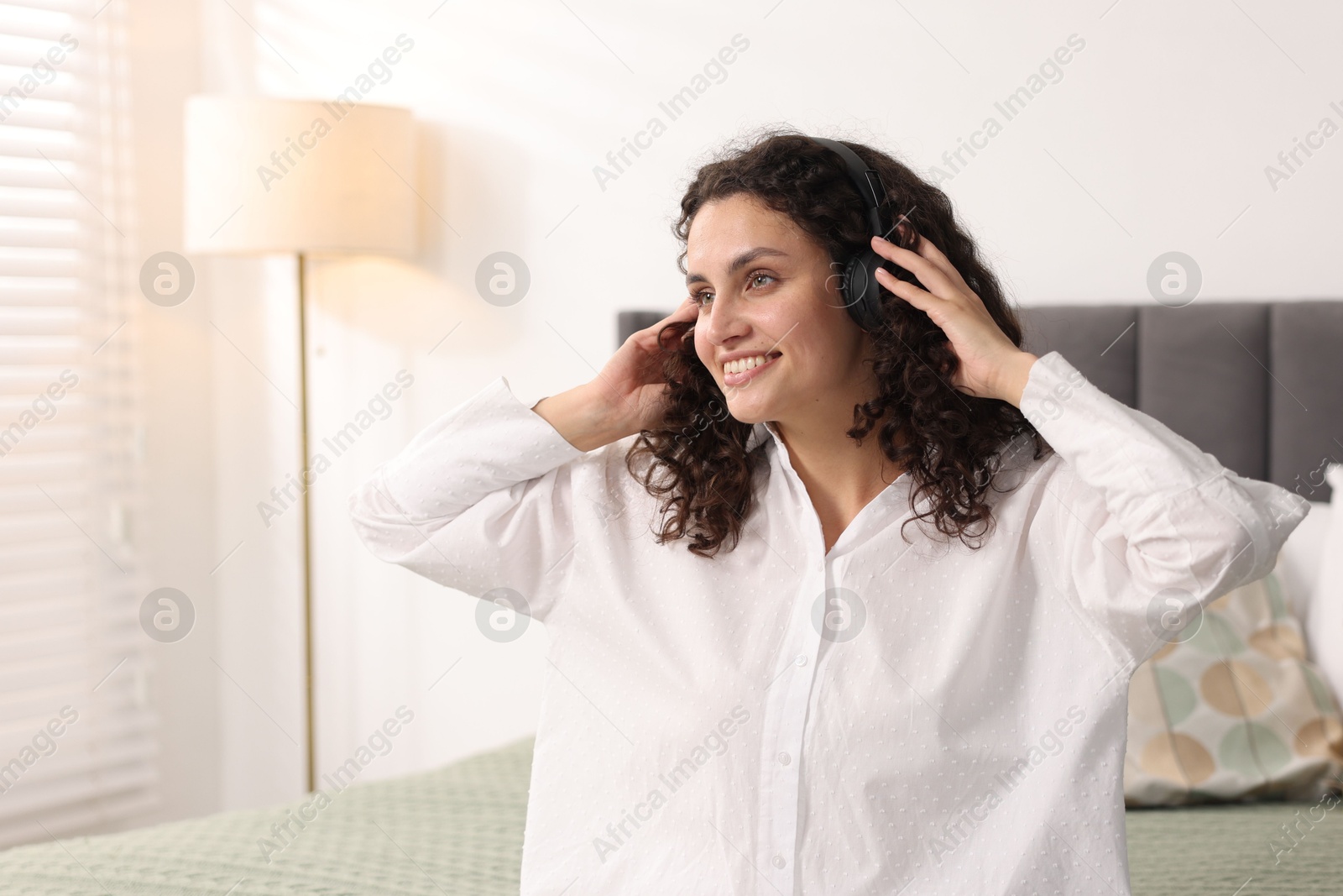 Photo of Young woman with headphones listening to music on bed at home
