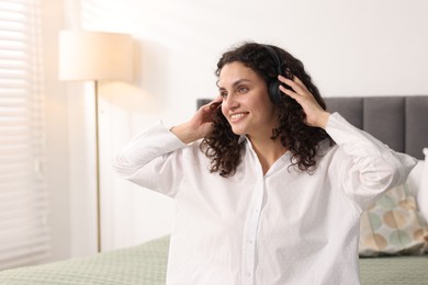Photo of Young woman with headphones listening to music on bed at home