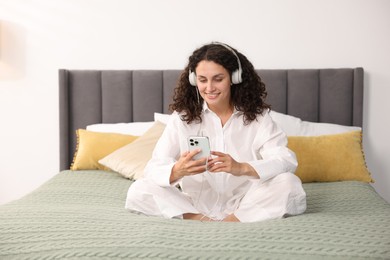 Photo of Young woman with headphones and smartphone listening to music on bed at home