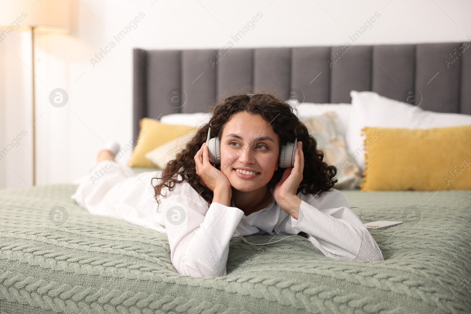 Photo of Young woman with headphones listening to music on bed at home