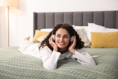Photo of Young woman with headphones listening to music on bed at home