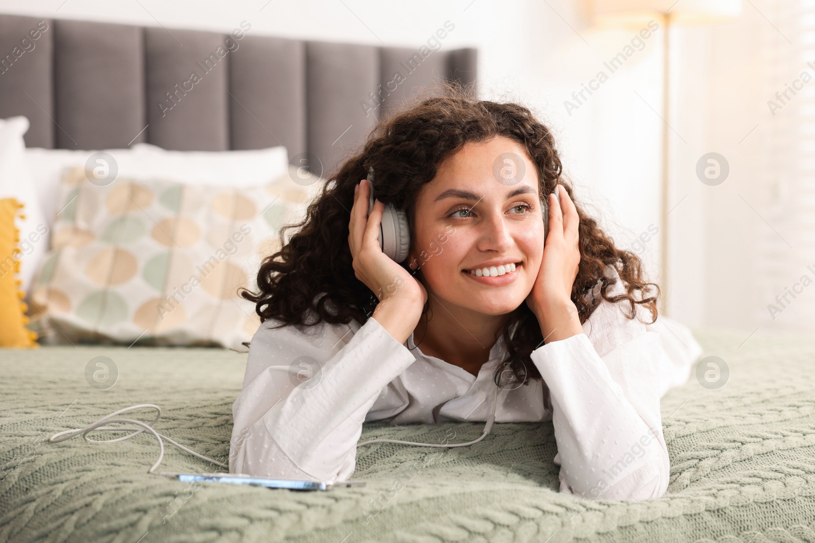 Photo of Young woman with headphones listening to music on bed at home