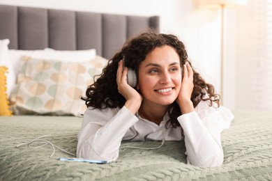Photo of Young woman with headphones listening to music on bed at home