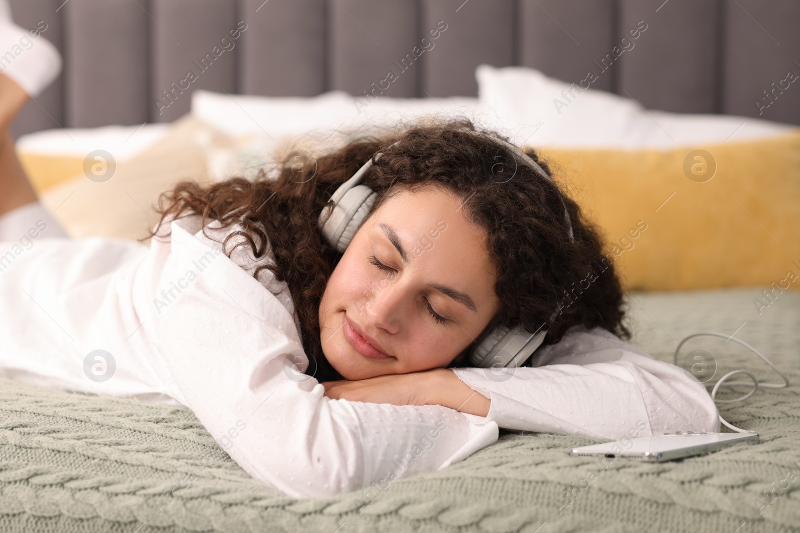 Photo of Young woman with headphones listening to music on bed at home
