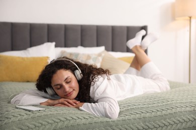 Photo of Young woman with headphones listening to music on bed at home