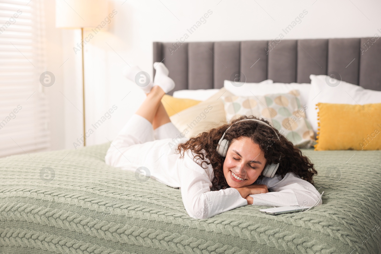 Photo of Young woman with headphones listening to music on bed at home