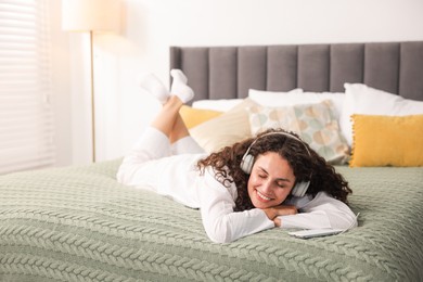 Photo of Young woman with headphones listening to music on bed at home