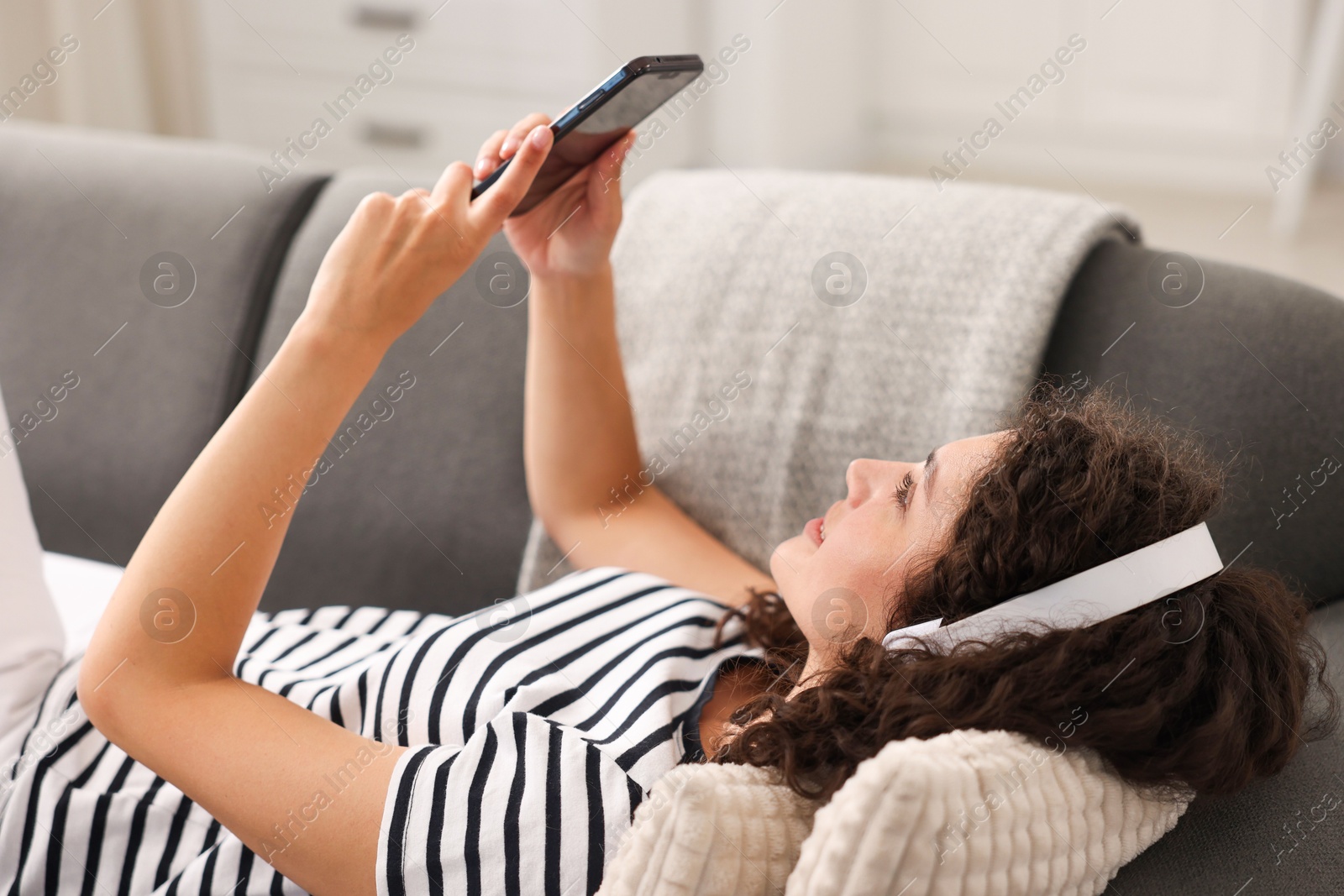 Photo of Young woman with headphones and smartphone listening to music at home