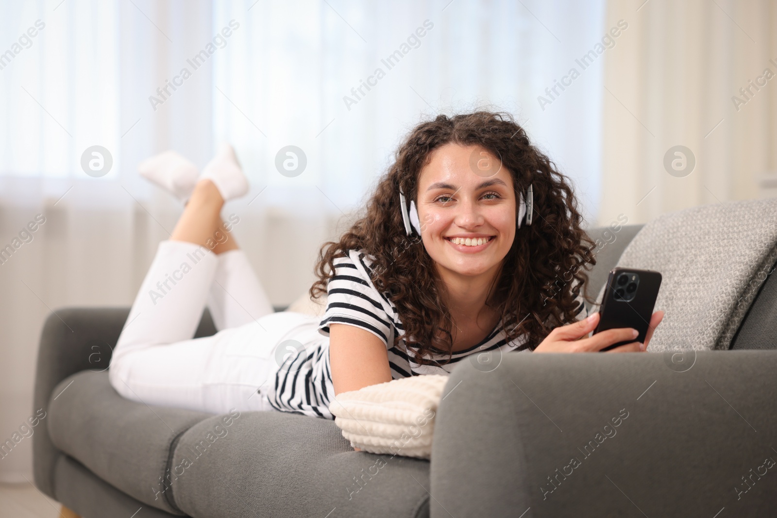 Photo of Young woman with headphones and smartphone listening to music at home