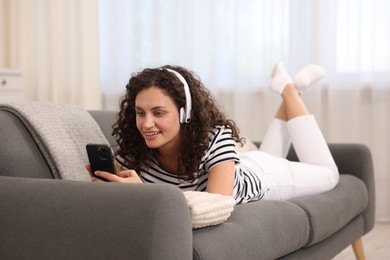 Photo of Young woman with headphones and smartphone listening to music at home