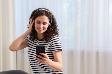 Photo of Young woman with headphones and smartphone listening to music at home, space for text