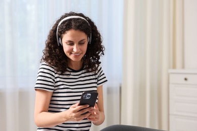 Photo of Young woman with headphones and smartphone listening to music at home, space for text