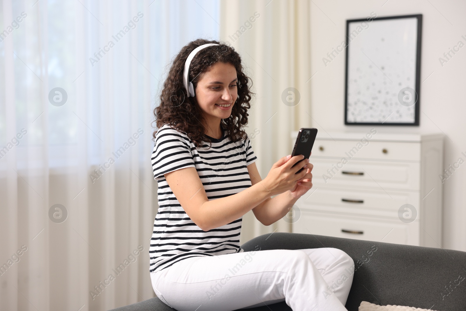 Photo of Young woman with headphones and smartphone listening to music at home