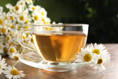 Photo of Aromatic tea in glass cup and chamomile flowers on wooden table, closeup