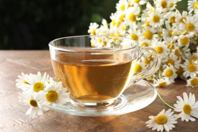 Photo of Aromatic tea in glass cup and chamomile flowers on wooden table, closeup
