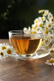 Photo of Aromatic tea in glass cup and chamomile flowers on wooden table, closeup