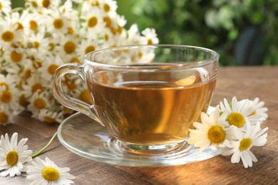 Photo of Aromatic tea in glass cup and chamomile flowers on wooden table, closeup