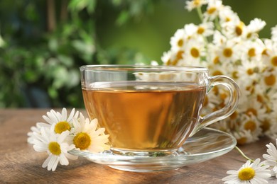 Photo of Aromatic tea in glass cup and chamomile flowers on wooden table, closeup
