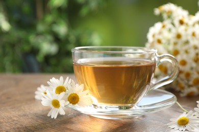 Photo of Aromatic tea in glass cup and chamomile flowers on wooden table, closeup