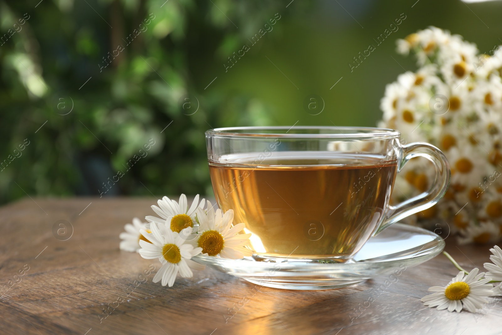 Aromatic tea in glass cup and chamomile flowers on wooden table, closeup Photo of Aromatic tea in glass cup and chamomile flowers on wooden table, closeup