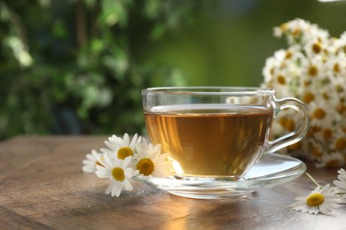 Photo of Aromatic tea in glass cup and chamomile flowers on wooden table, closeup
