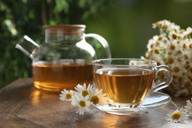 Photo of Aromatic tea in glass cup and chamomile flowers on wooden table, closeup