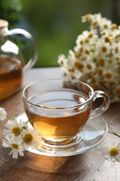 Photo of Aromatic tea in glass cup and chamomile flowers on wooden table, closeup