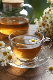 Photo of Aromatic tea in glass cup and chamomile flowers on wooden table, closeup