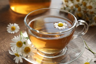 Photo of Aromatic tea in glass cup and chamomile flowers on wooden table, closeup