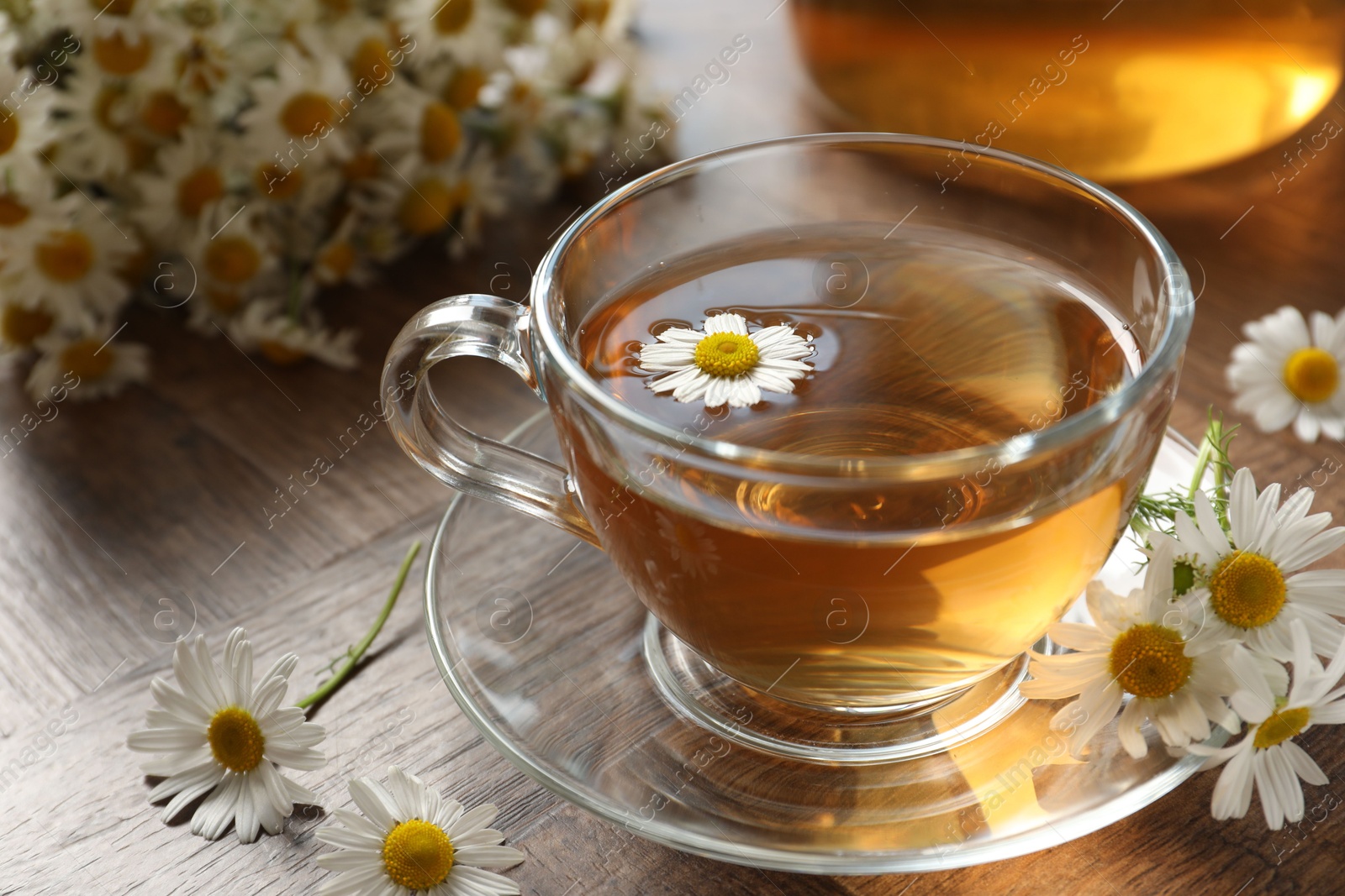Aromatic tea in glass cup and chamomile flowers on wooden table, closeup Photo of Aromatic tea in glass cup and chamomile flowers on wooden table, closeup