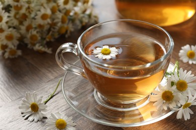 Photo of Aromatic tea in glass cup and chamomile flowers on wooden table, closeup